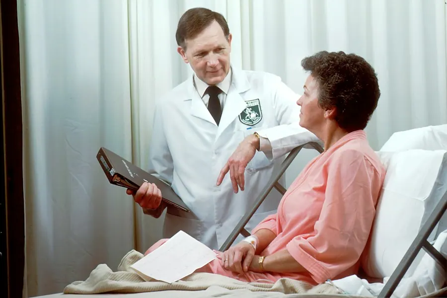 Internist holding a chart while talking with a patient sitting up in a hospital bed, internal medicine billing services