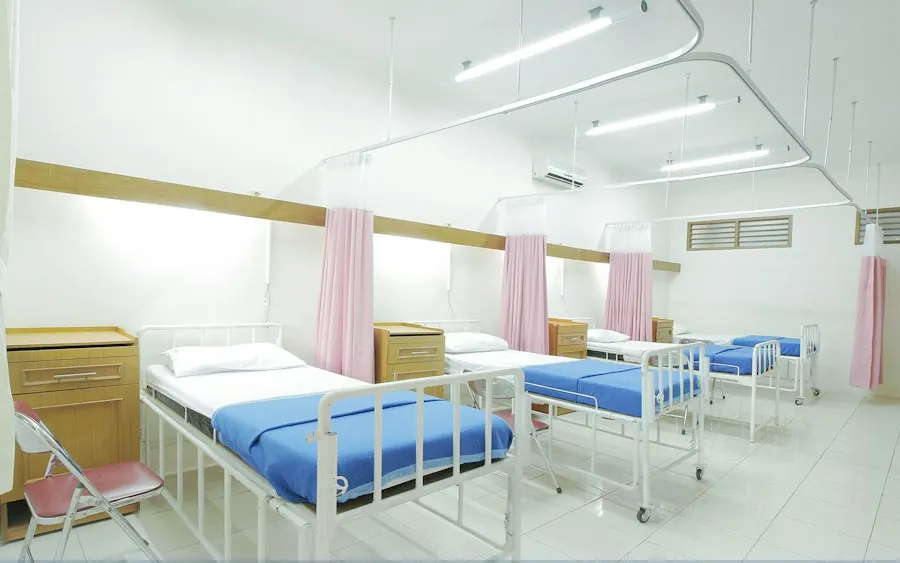 Row of empty treatment beds with pink privacy curtains in a brightly lit clinic bay, urgent care billing services